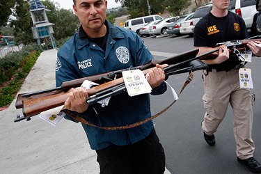 LAPD Officer Tony Lobato, left, of the Harbor Division, and ATF Special Agent Christian Hoffman carry some of the confiscated weapons at the Harbor Station in San Pedro.