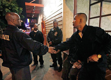 In this photo taken Feb. 26, 2010, Aquil Basheer, left, of the Professional Community Intervention Training Institute greets a pedestrian, as he gives a tour, outside the The Cottage bar where one of his intervention workers, Ronnie "Looney" Barron, was killed in a drive-by shooting on Feb. 7, 2010, in Los Angeles.