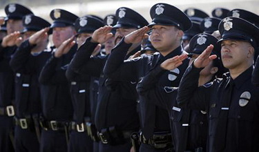 Officers salute as they watch the funeral of police Officer Ryan Bonaminio broadcast on a giant screen to an overflow crowd of mourners in Riverside, Calif., on Nov. 16. Bonaminio was shot and killed on Nov. 7 after he pulled over the driver of a stolen big-rig cab.